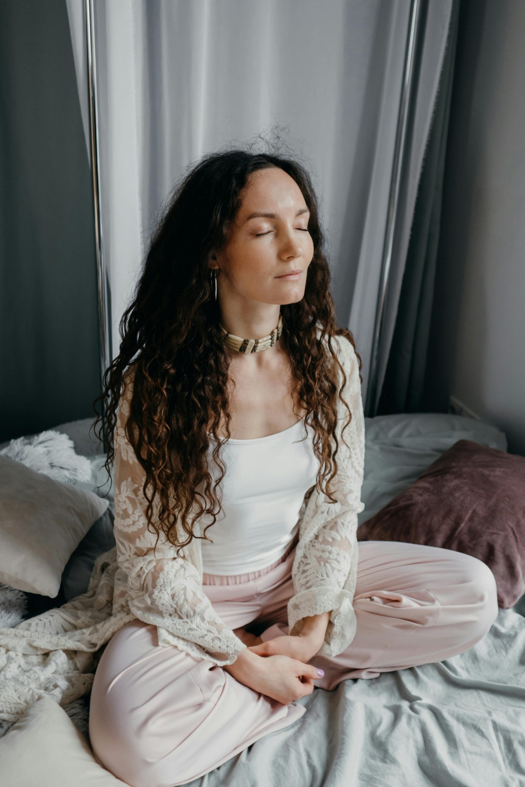 A serene woman meditates indoors on a bed, embodying tranquility and mindfulness.